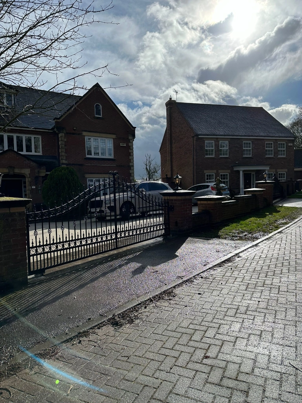 Decorative front drive way access gates, black powered gates mounted on side brick pillars, left hand view.