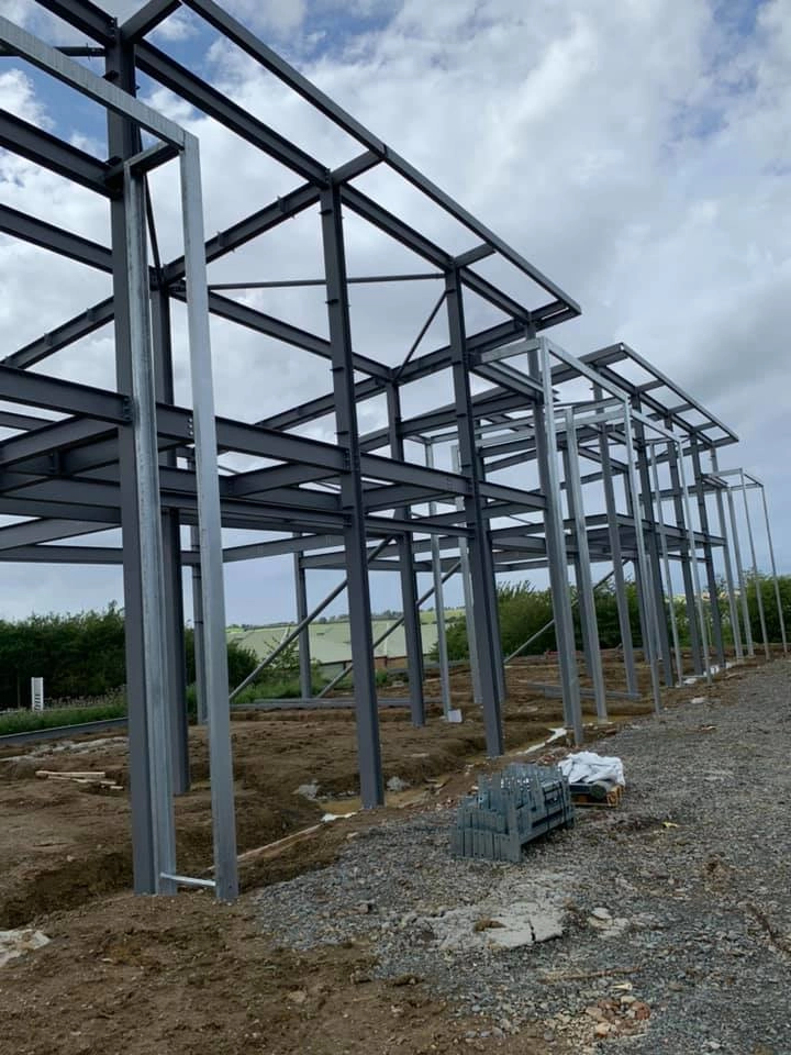 showing the structural steel skeleton or as its called portal frame) of the building currently under construction. This framework utilizes pre-fabricated steel beams to form the structural backbone of the building.