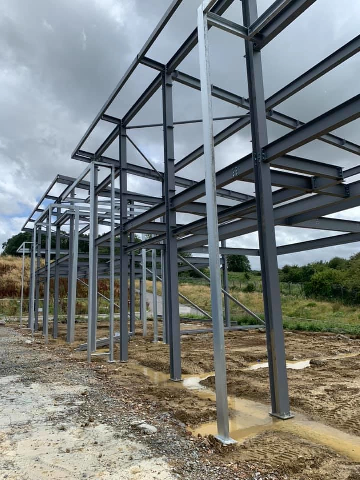 showing the structural portal frame sat on its foundations, The framework utilizes Diagonal steel rods that form an "X" shape between bays to provide lateral stability against wind and movement.