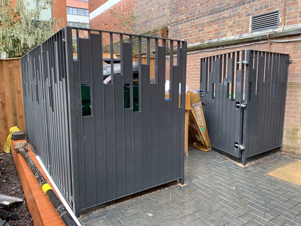 A waste are barrier to section off this area from the public, with gates that allow easy access and extraction of waste bins.
